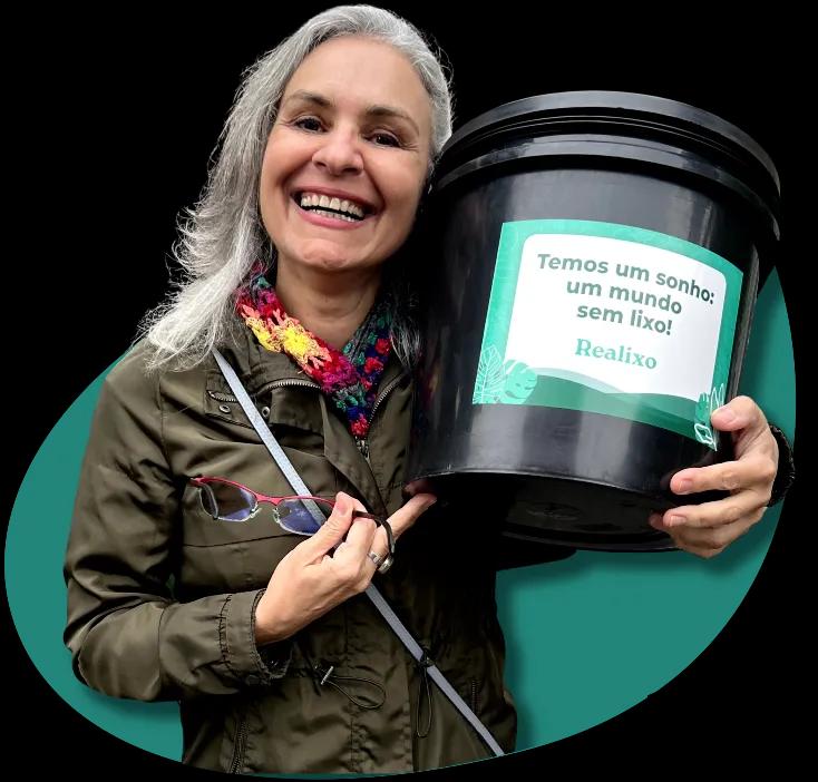 Uma mulher com cabelos brancos em pé, segurando perto da cabeça um balde escrito Temos um sonho, um mundo sem lixo, atrás dela está um fundo verde